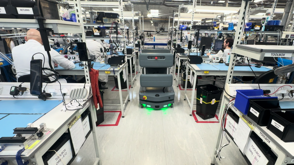Autonomous vehicle operating between manufacturing workstations while employees carry out production tasks.