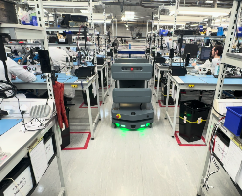 Autonomous vehicle operating between manufacturing workstations while employees carry out production tasks.